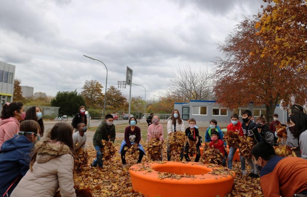 Foto: Schülerinnen und Schüler werfen im Kreis stehend Herbstlaub in die Luft