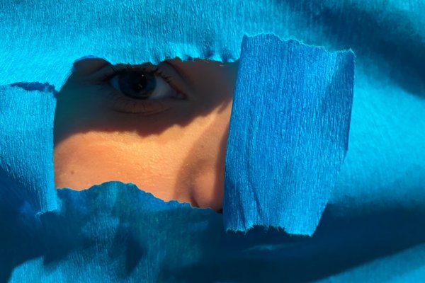 Foto: ein Kind schaut von hinten durch ein Loch in blauem Papier